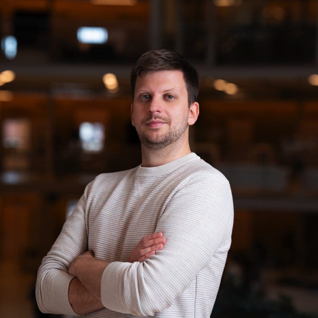 Noyan poses for a portrait image - his hands are crossed in front of his chest. He wears a long sleeve white shirt.